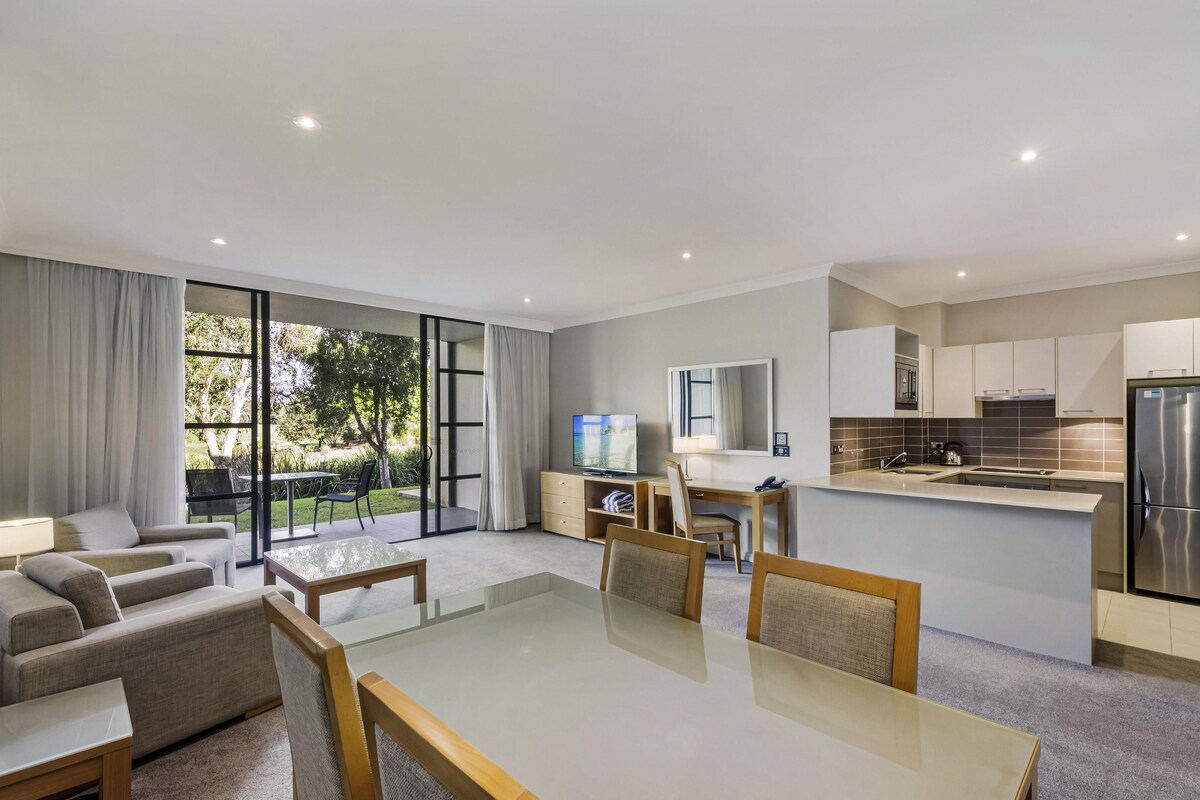 Une chambre d’hôtel moderne dotée d’un coin repas, d’une cuisine et d’une porte-fenêtre coulissante donnant sur un jardin.