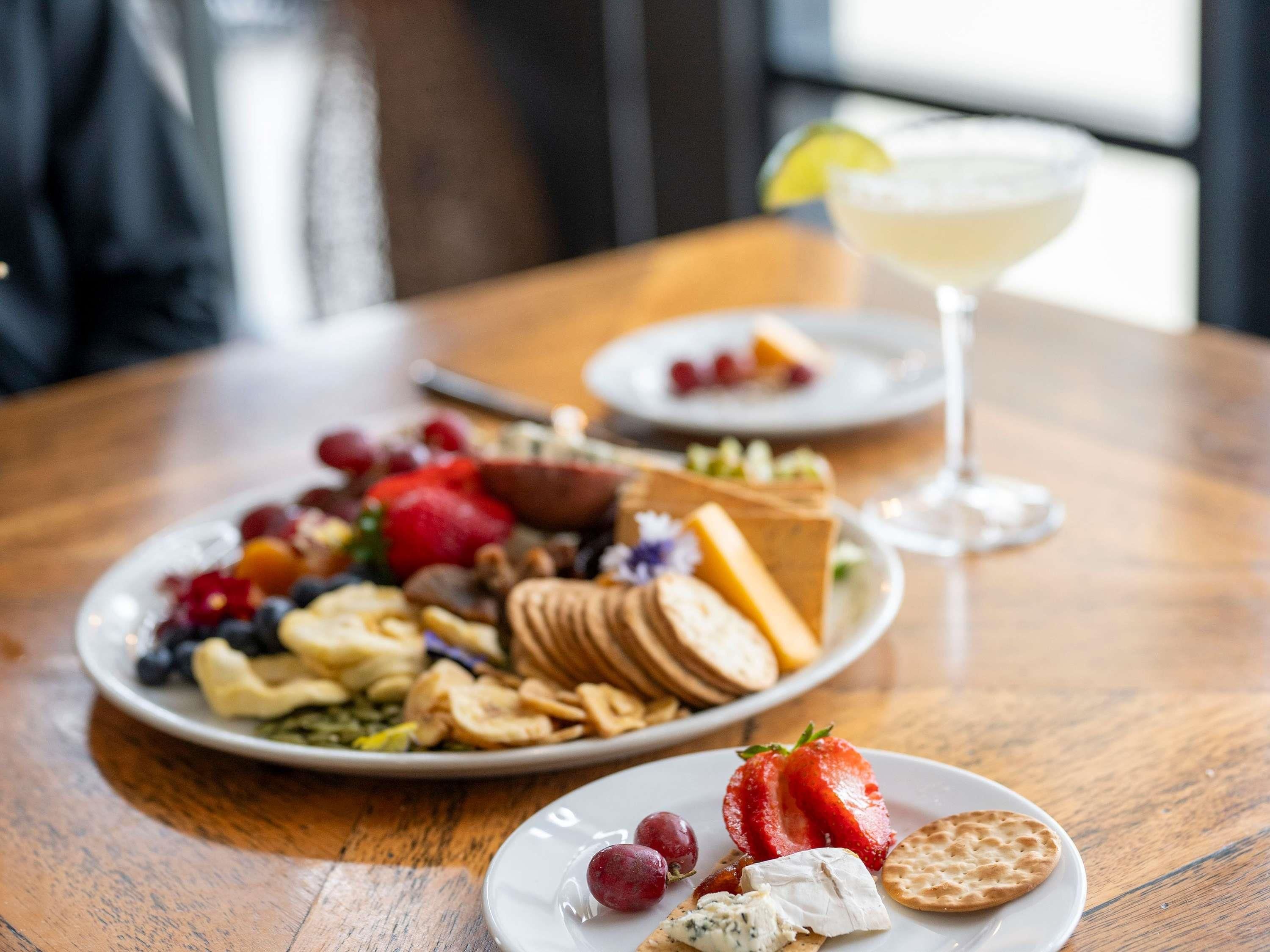 Una mesa con un plato de quesos variados, frutas y galletas.