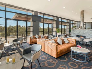 A spacious lounge area with leather sofas, round tables, and a stone fireplace. - Mercure Kooindah Waters Central Coast (Wyong)