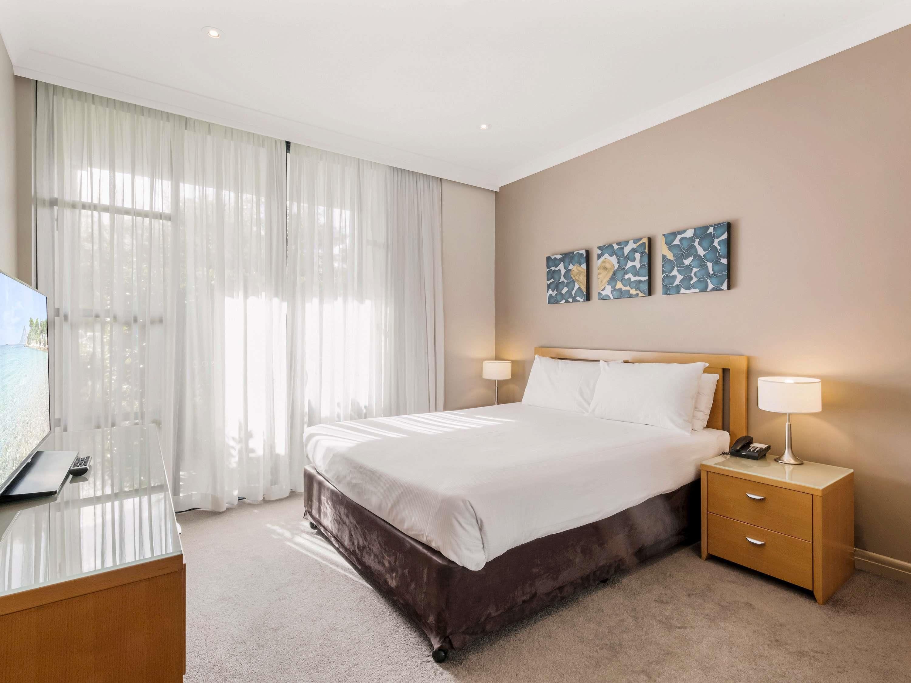 Habitación de hotel con cama, lámparas de noche, escritorio con computadora portátil y televisor.