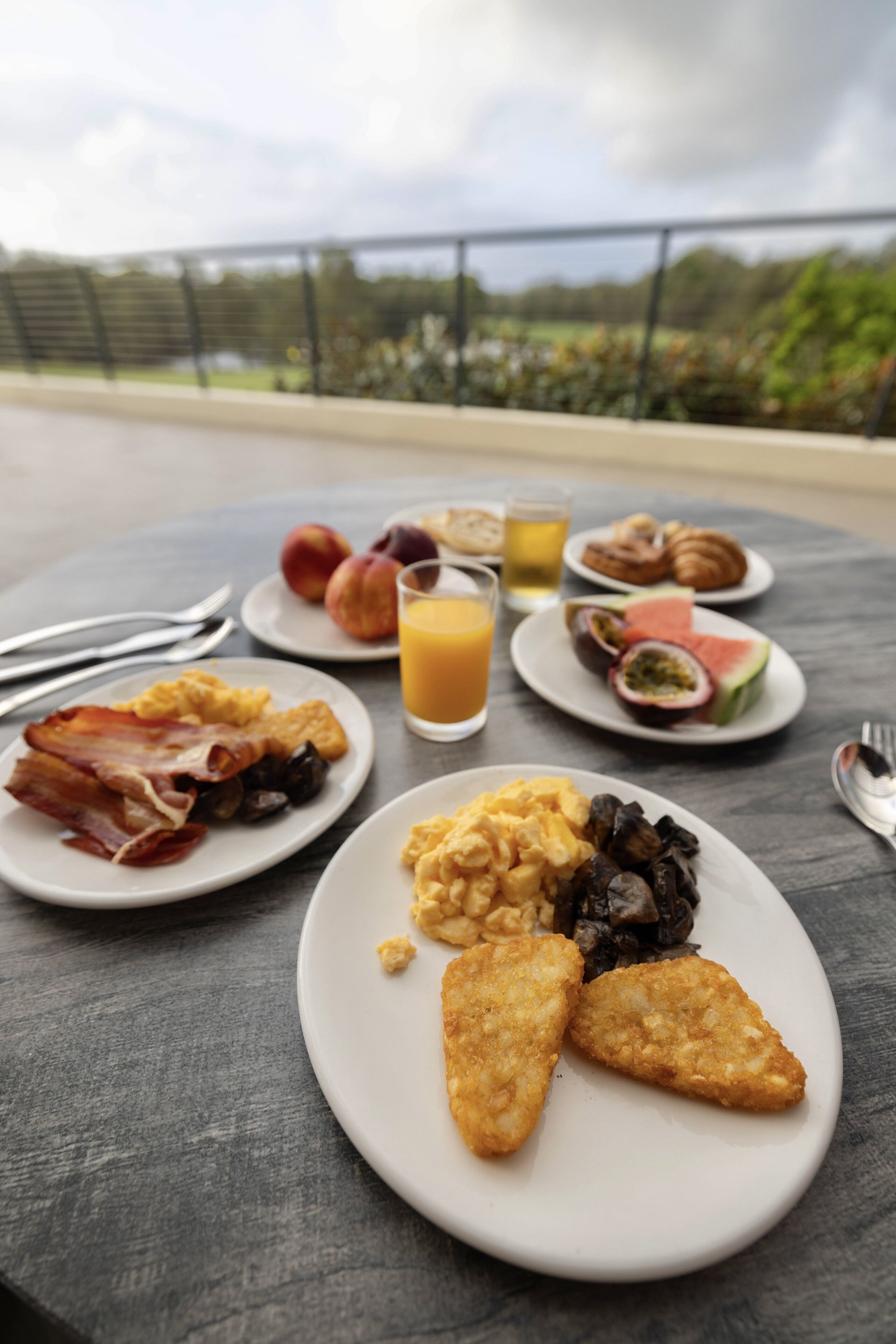 A breakfast table with plates of eggs, bacon, toast, and fruit, and a glass of orange juice.