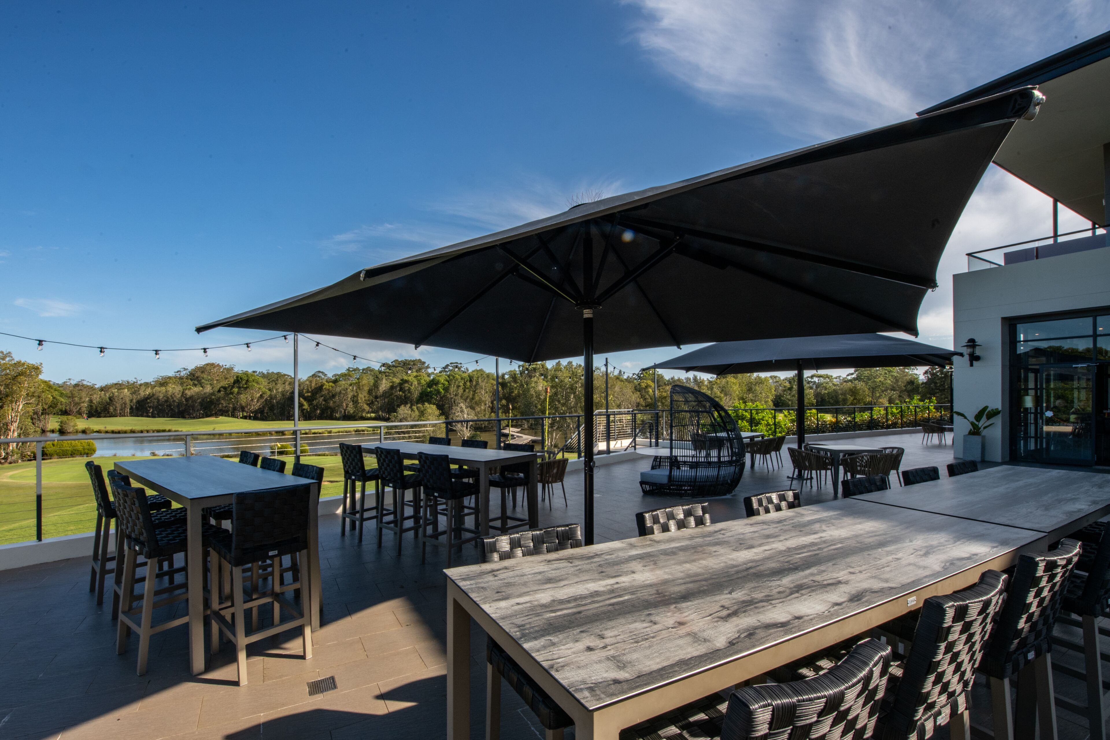 Un espace extérieur aménagé en terrasse, avec une grande table et des chaises, un coin salon abrité et une vue sur un terrain de golf.