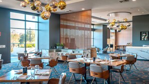 Ein moderner Hotel-Speiseraum mit mehreren Tischen und Stühlen, großen Fenstern und dekorativen, kugelförmigen Leuchten.
