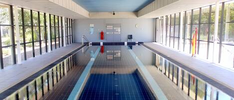 A large indoor swimming pool with clear glass walls, a tiled floor, and a visible exit door.