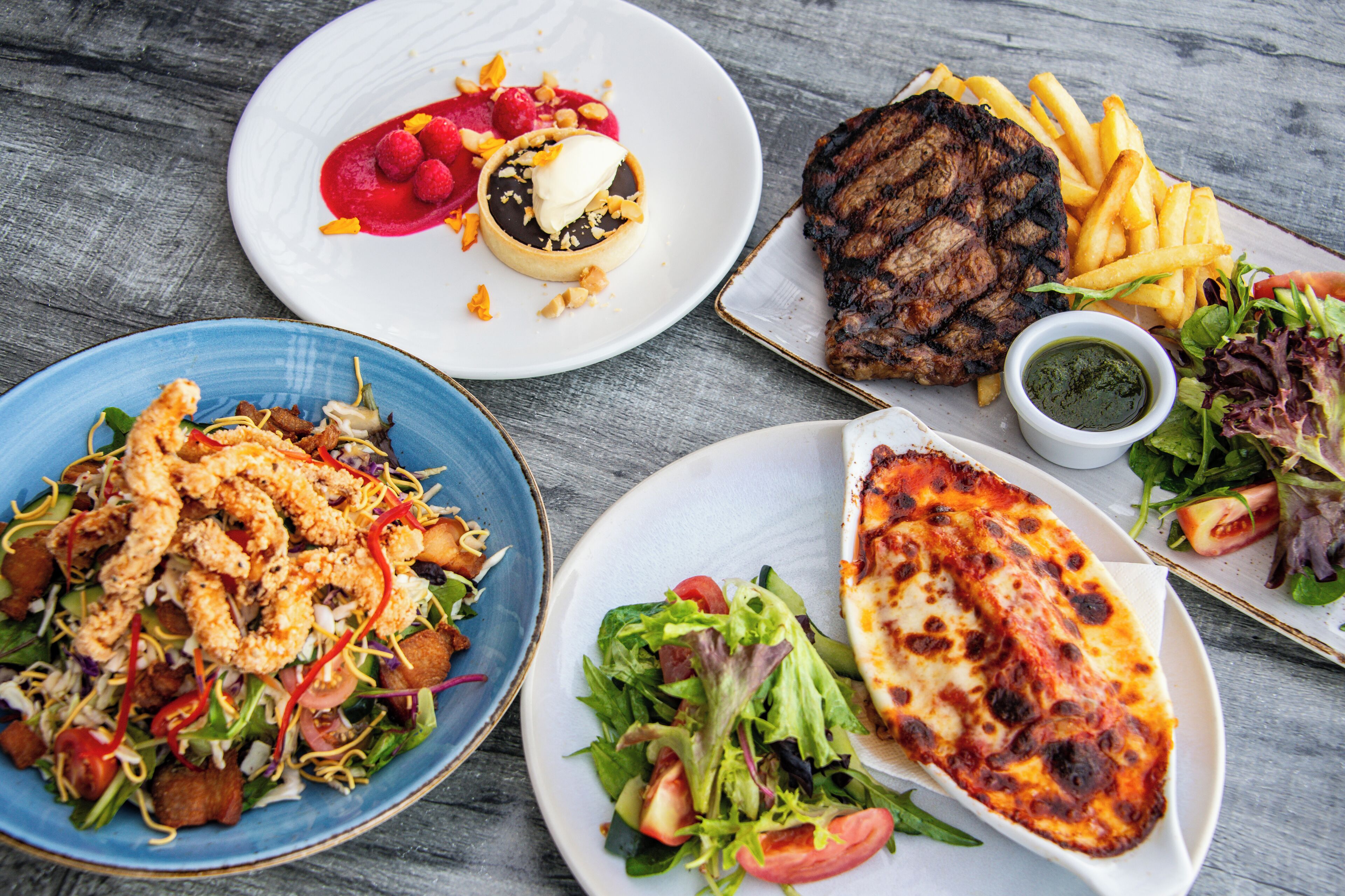 A variety of dishes including grilled steak, fries, a salad, and a seafood dish.