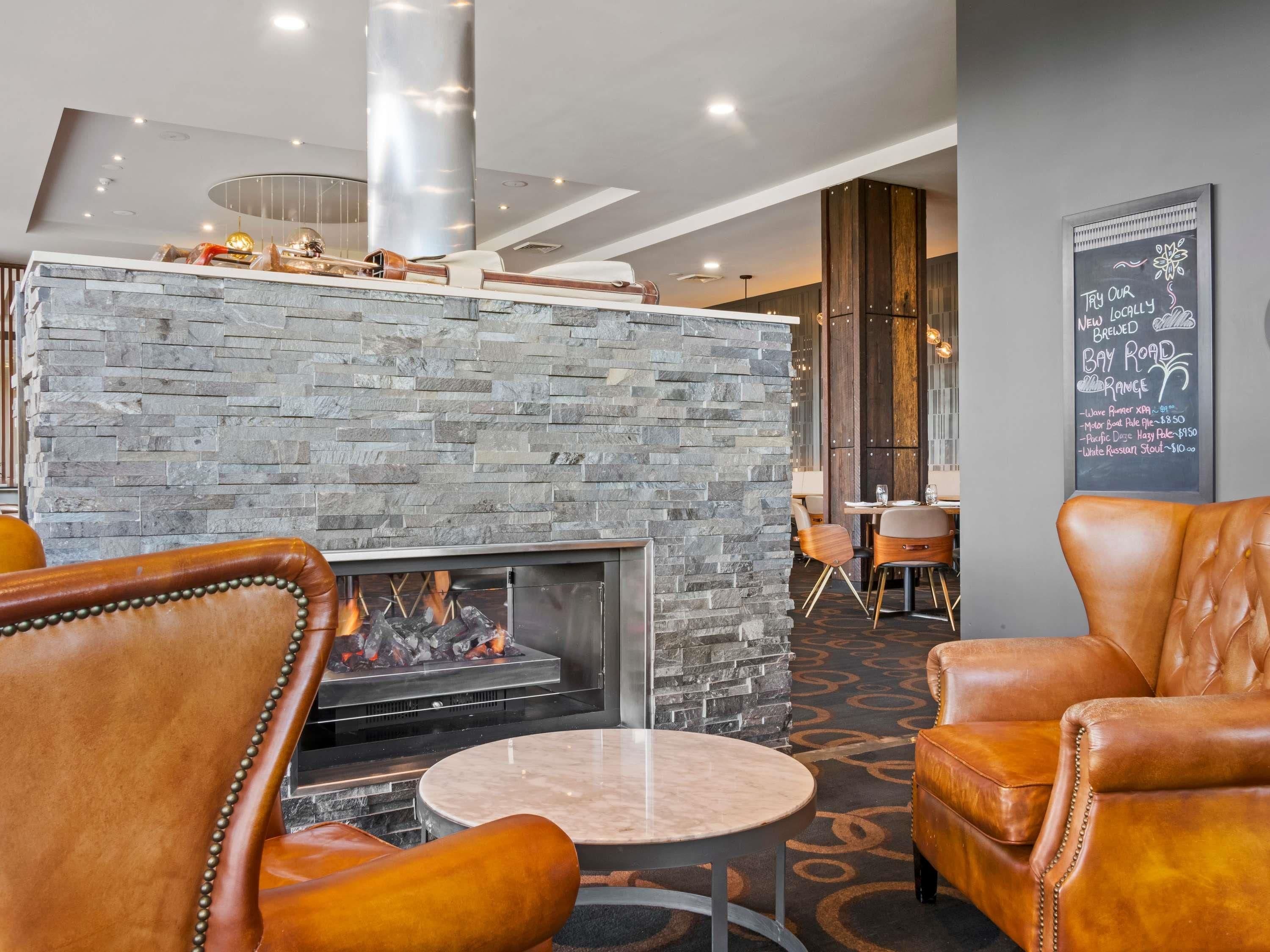 Ein moderner Lounge-Bereich mit Kamin aus Stein, Ledersitzgelegenheiten und einer Speisekarte an der Wand.
