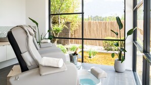 Une salle de spa moderne équipée d’une table de massage, d’un petit bassin et offrant une vue sur le jardin.
