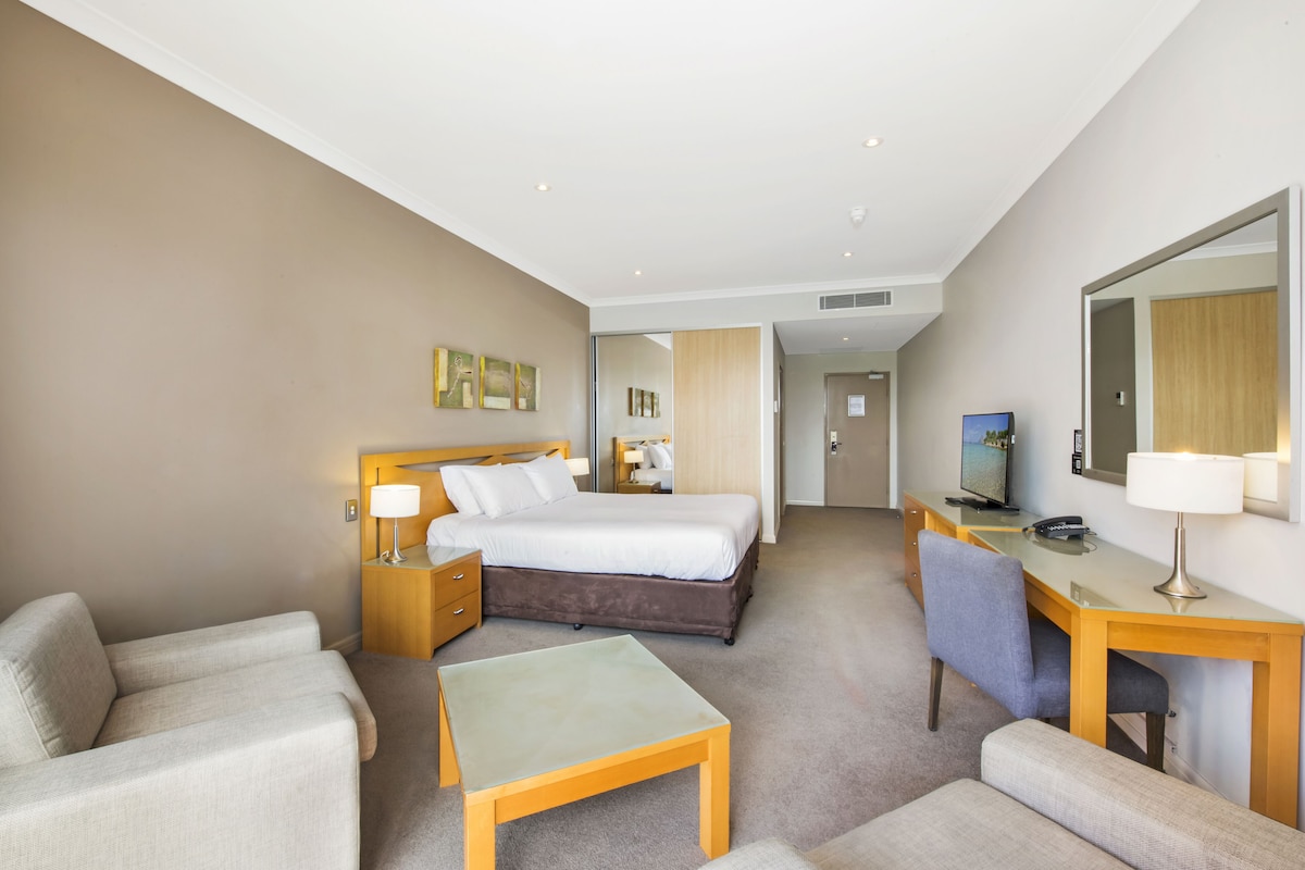 Una habitación de hotel con cama, escritorio, silla, sofá y televisión.