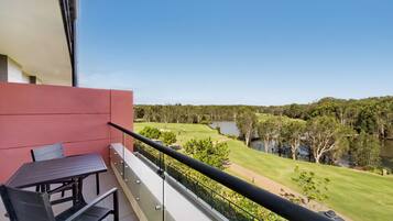 A balcony with a table and chairs, overlooking a golf course and a lake.