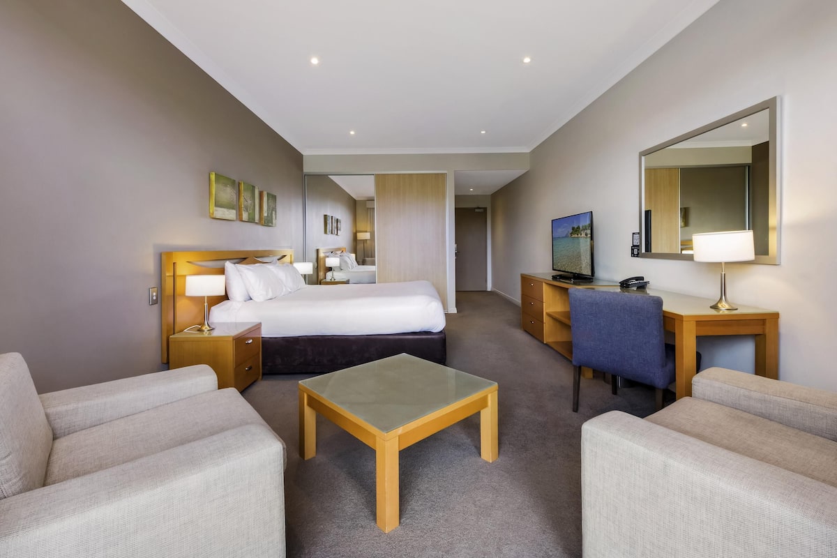 Ett hotellrum med en säng, ett skrivbord, en stol, ett litet bord och en tv.