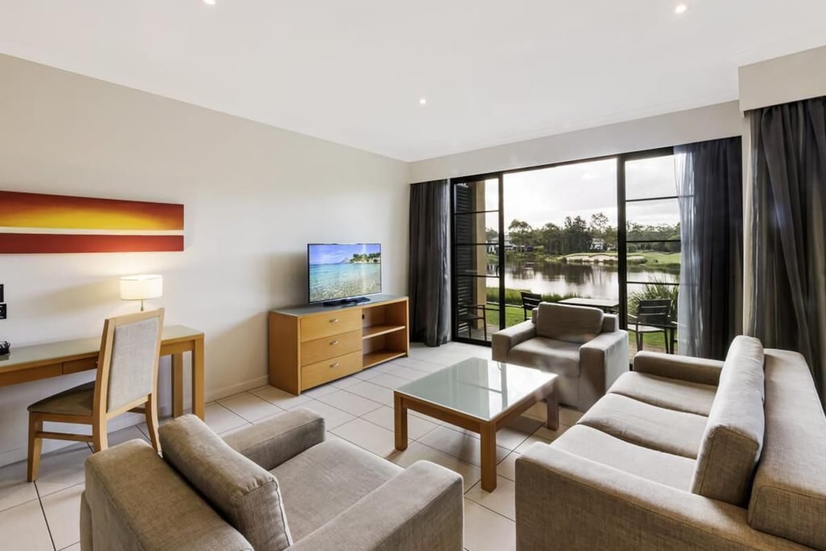 Una sala de estar moderna con televisor, sofá, mesa de centro y vista a un lago.