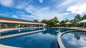 Une piscine à bord incurvé, entourée de chaises longues et de parasols, et un bâtiment avec de grandes fenêtres en arrière-plan.
