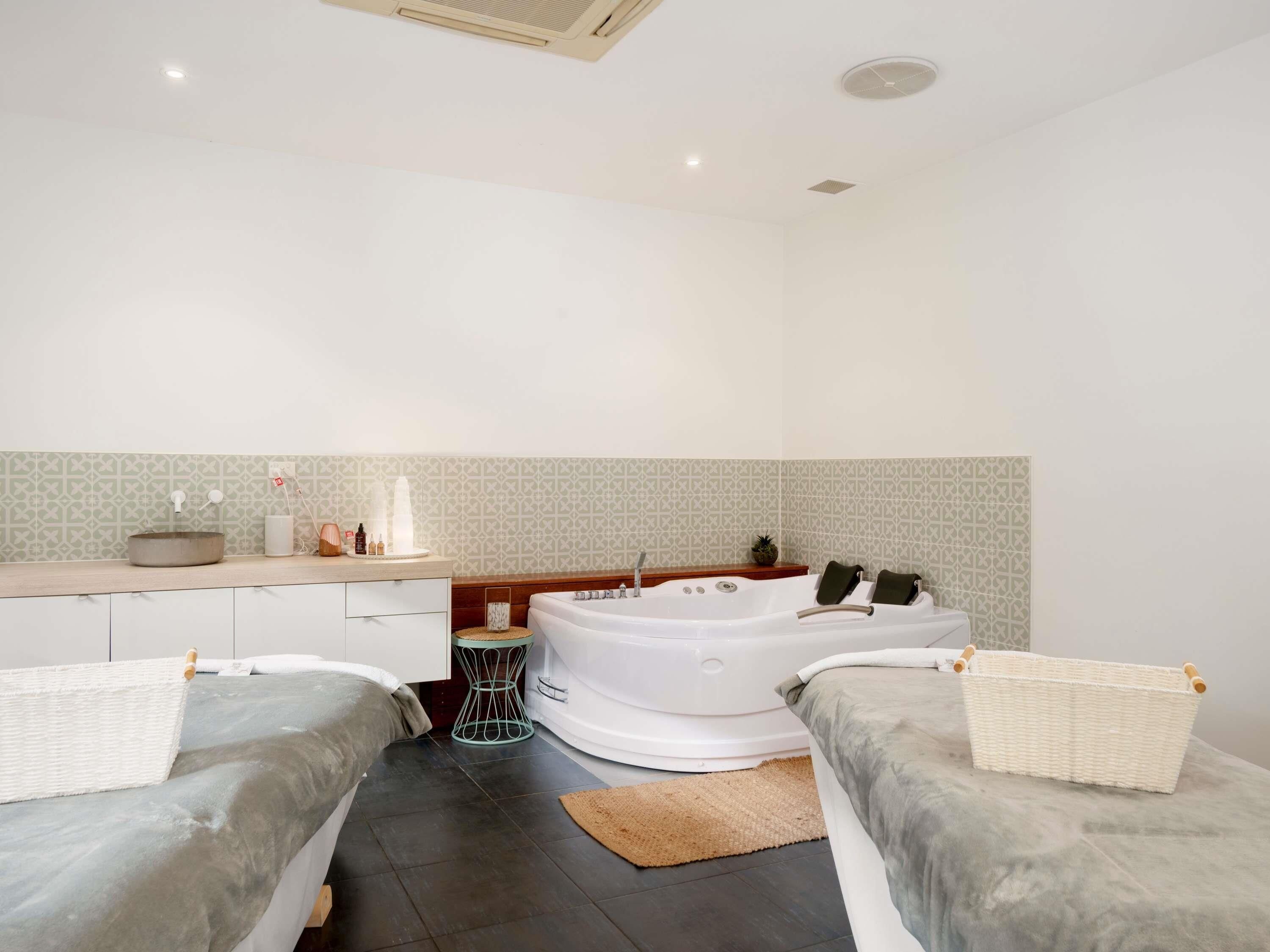A modern bathroom with a bathtub, two bedside tables, a sink, and a mirror.