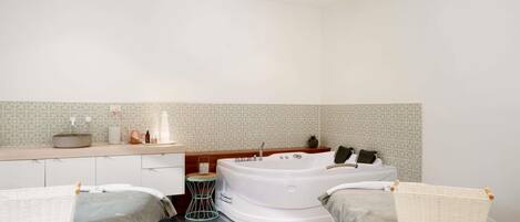 A modern bathroom with a bathtub, two bedside tables, a sink, and a mirror.