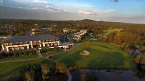 Vue aérienne d’un terrain de golf avec un club-house, des plans d’eau et une végétation luxuriante environnante.