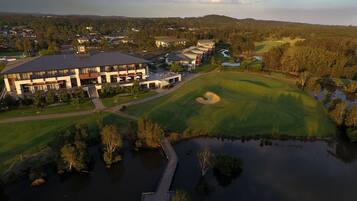 An aerial view of a golf course with a clubhouse, water bodies, and surrounding greenery.