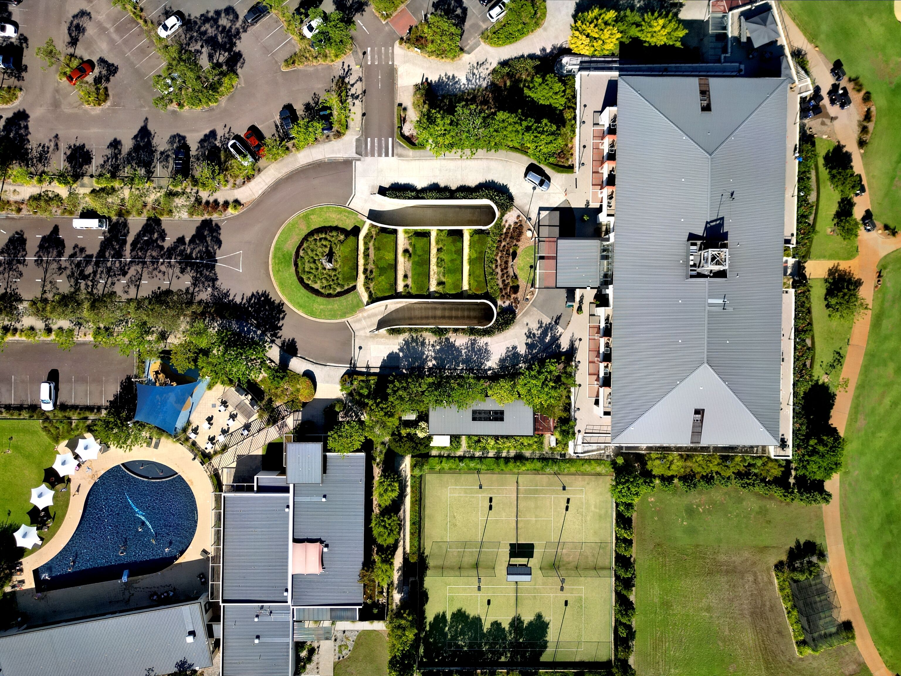 An aerial view of a residential area with a large house, a tennis court, a swimming pool, and a parking lot.