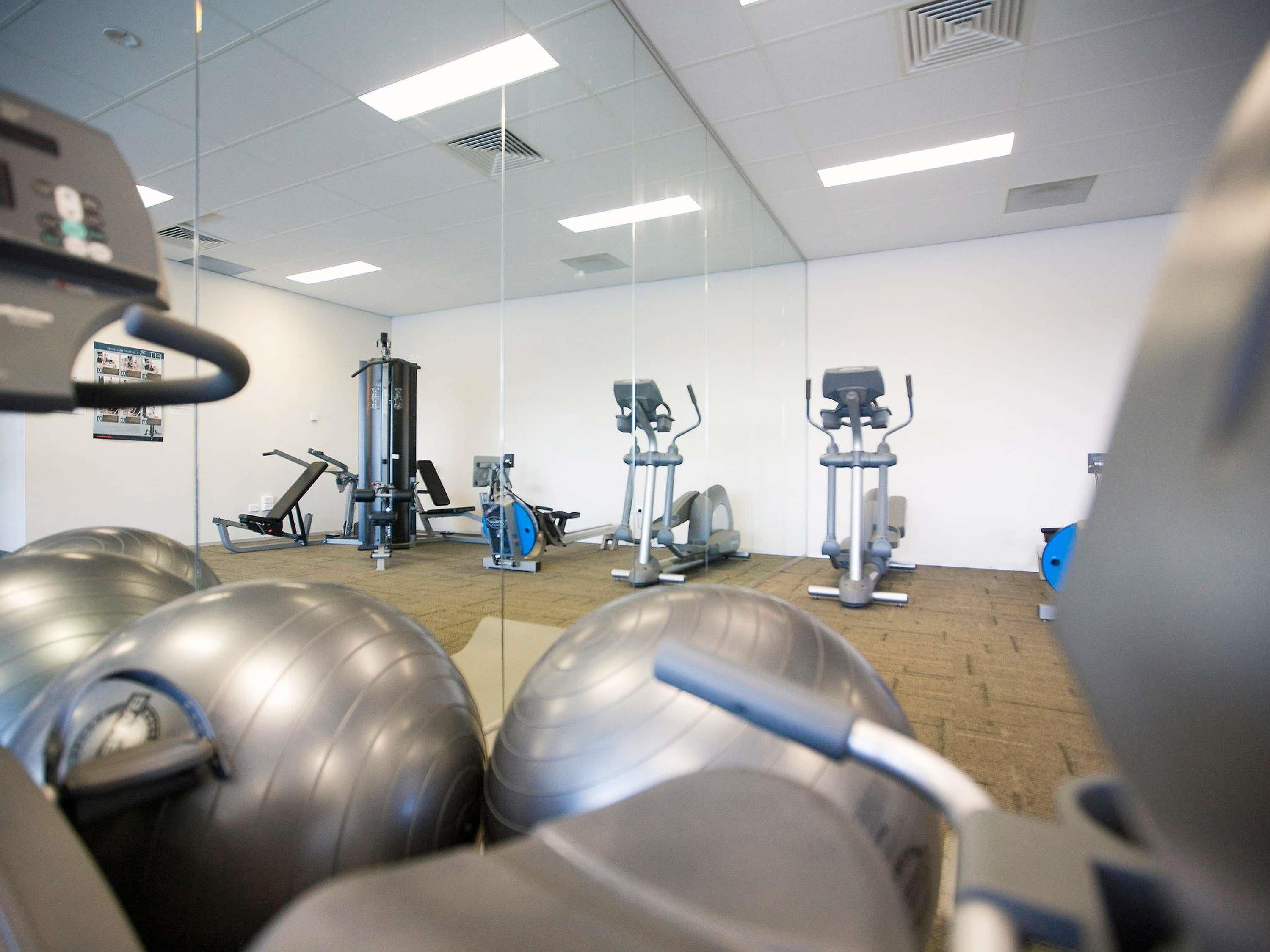 A gym with exercise equipment, a mirror wall, and a ceiling with lights.