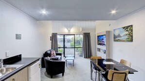 A modern hotel room with a kitchenette, a dining area with a table and chairs, a sofa, and a large window offering a view of the outdoors. - Arista of Rotorua (Rotorua)