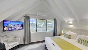 A hotel room with a bed, a TV mounted on the wall, a window with curtains, and a nightstand with a lamp. - Arista of Rotorua (Rotorua)