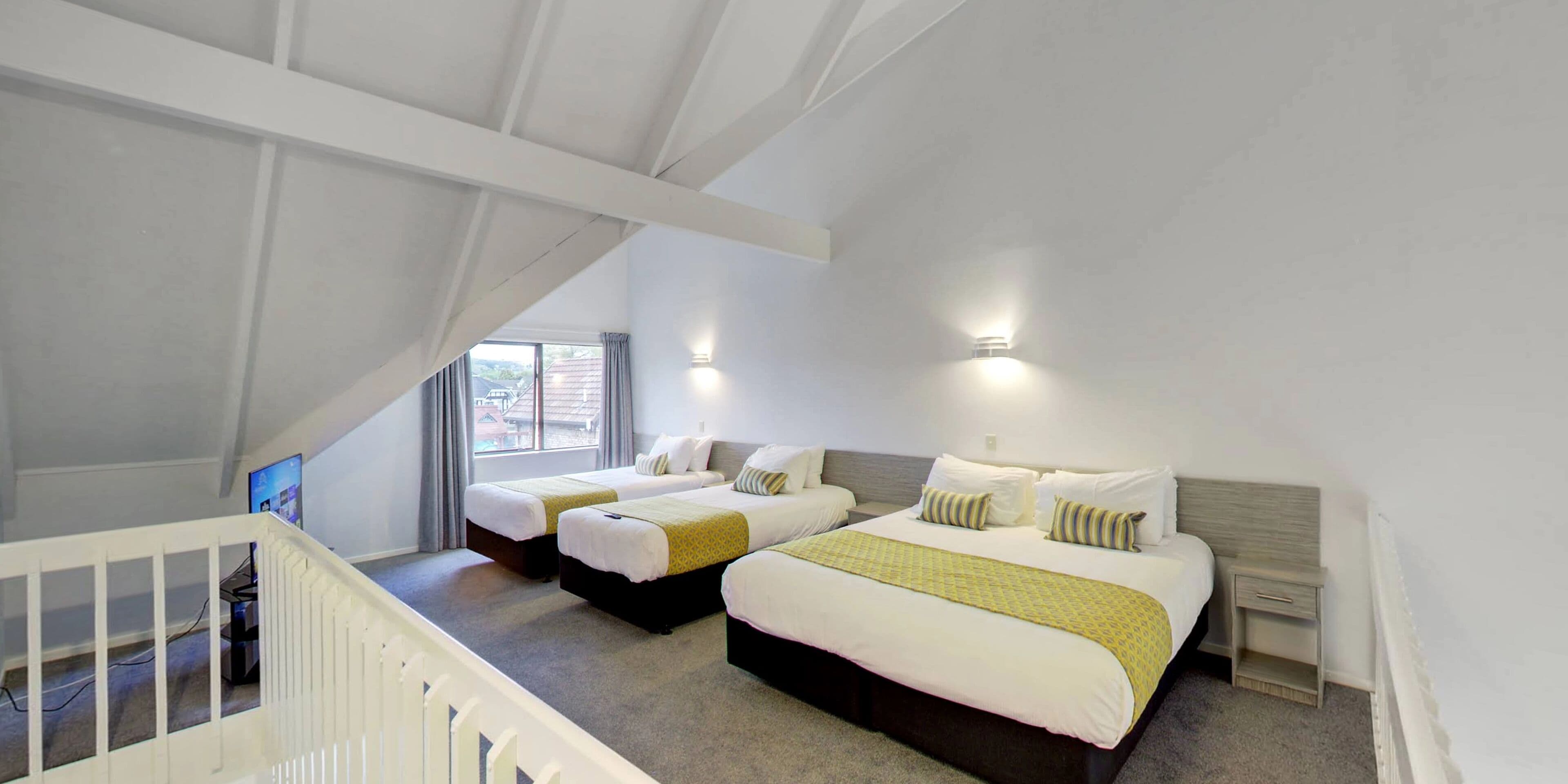 Habitación de hotel con dos camas, una escalera y un ventanal con cortinas.