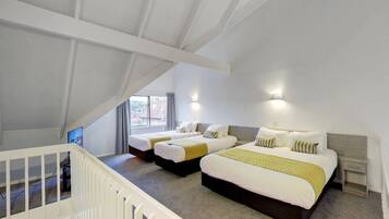 Habitación de hotel con dos camas, una escalera y un ventanal con cortinas.