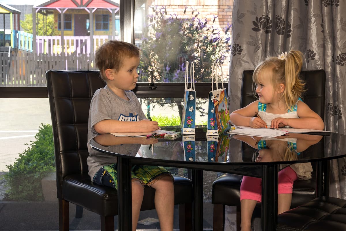 Dos niños sentados en una mesa de vidrio con vistas a edificios coloridos.