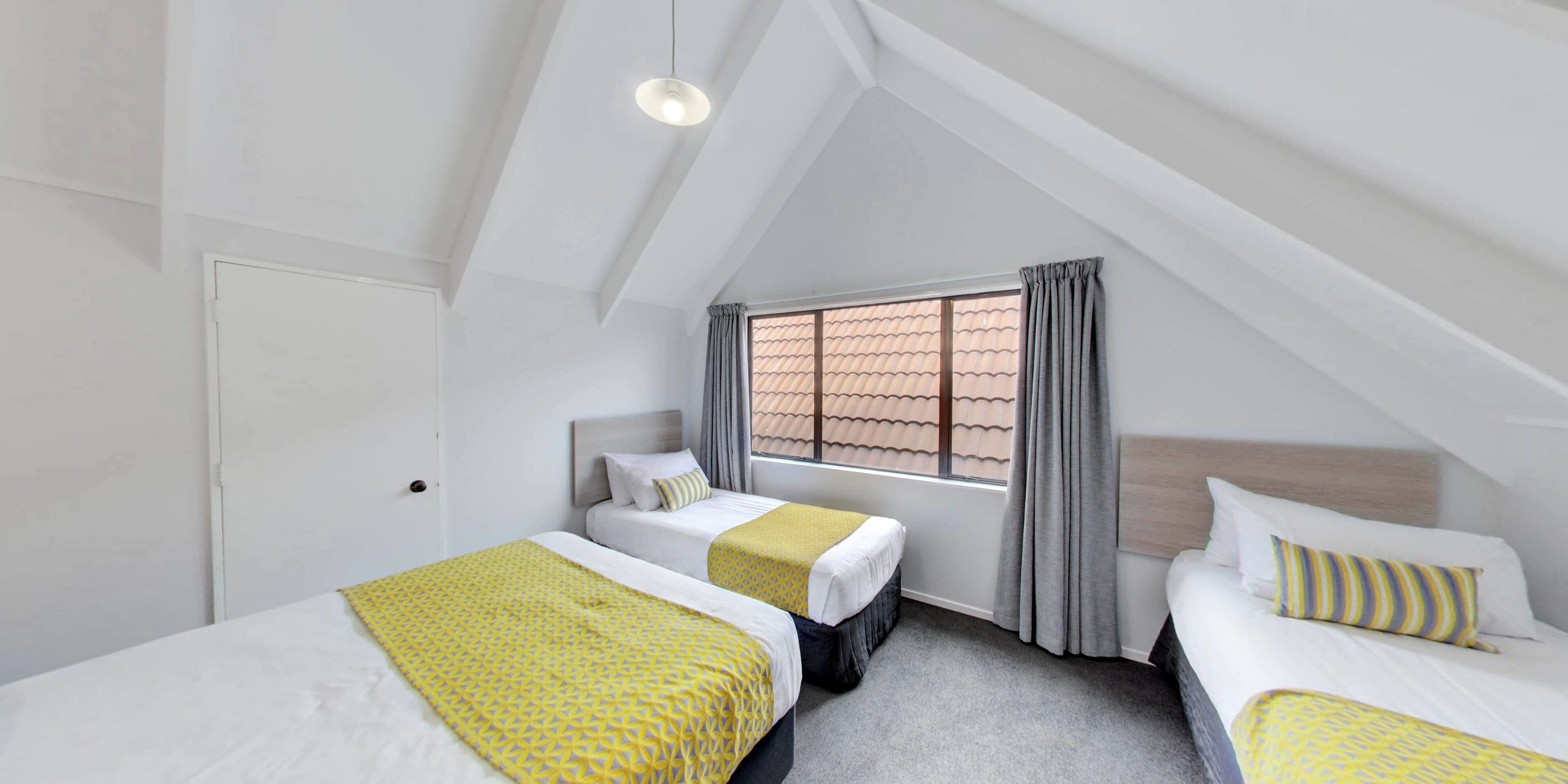 Ein Hotelzimmer mit zwei Betten, einem Fenster mit Vorhängen und einer geneigten Decke.