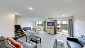 A modern living room with a glass coffee table, leather sofas, a flat-screen TV, and a dining area with chairs and a table. - Arista of Rotorua (Rotorua)