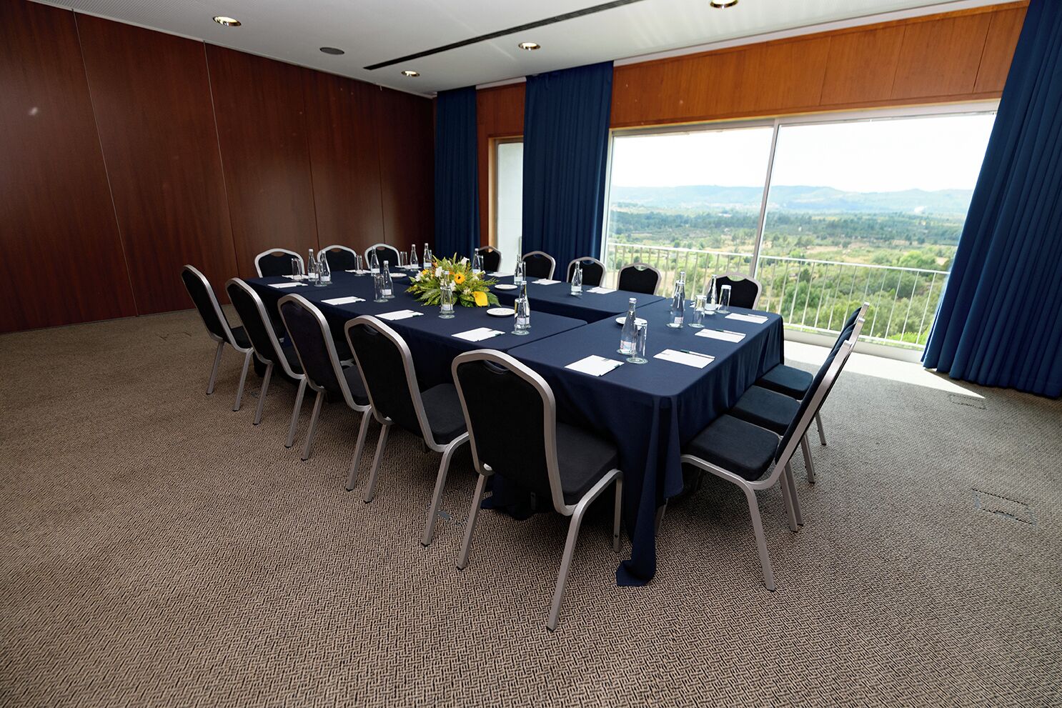 Un salón de conferencias con una larga mesa, sillas y vistas al paisaje a través de amplios ventanales.