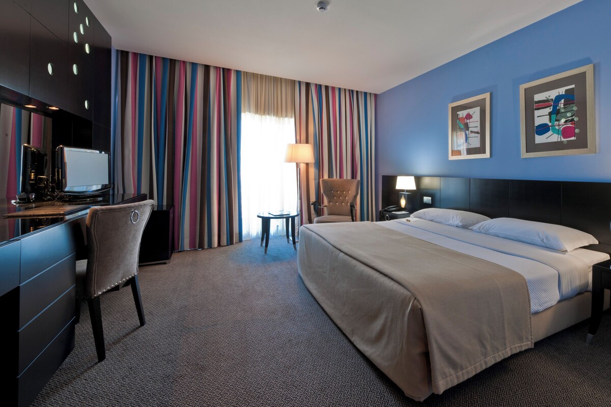 A hotel room with a bed, desk, chair, and two bedside lamps.