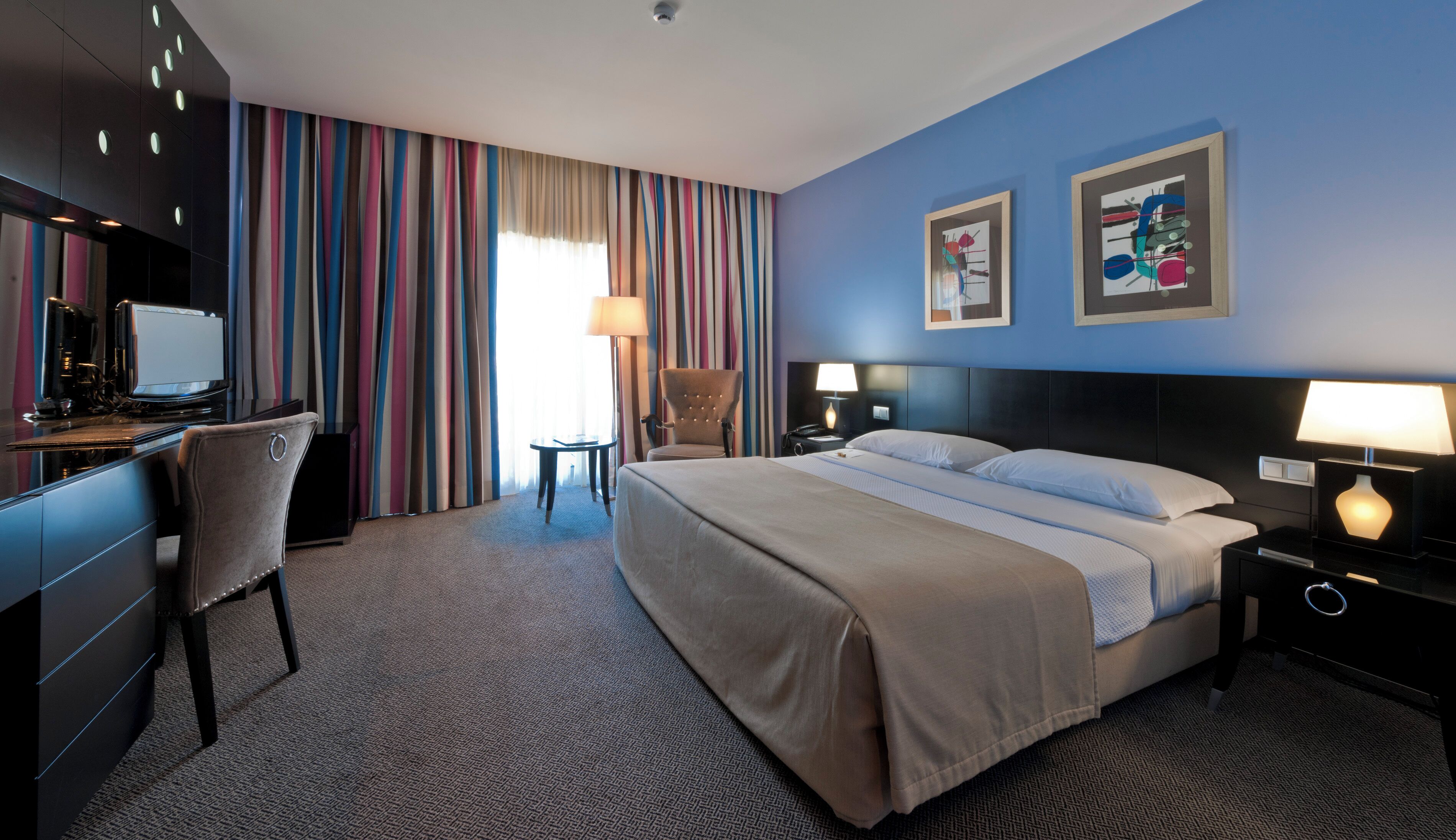 Une chambre d’hôtel équipée d’un lit, d’un bureau, d’une chaise et de deux lampes de chevet.