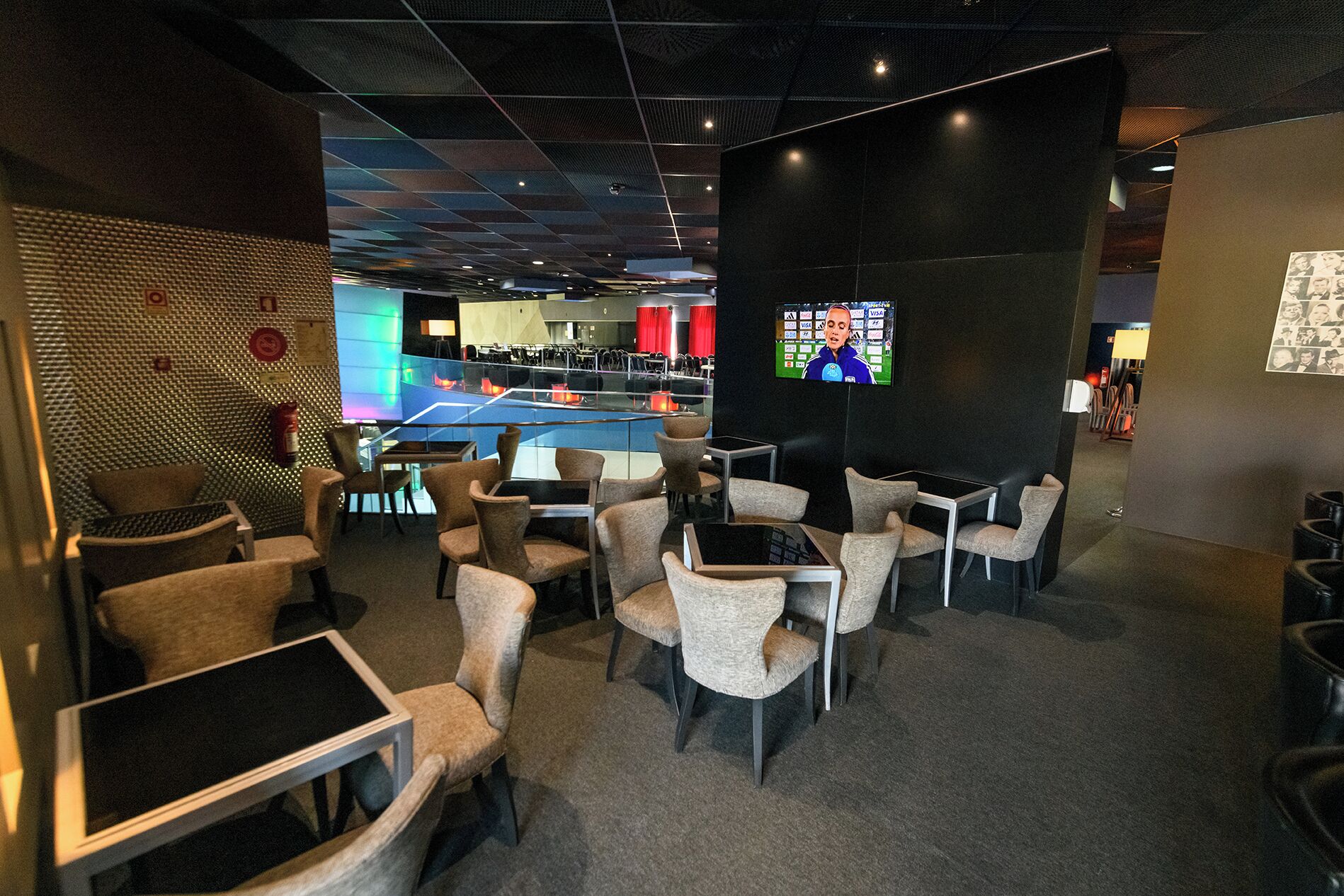 A modern lounge area with multiple seating options, a large screen for viewing, and a visible pool area in the background.