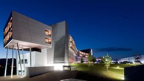 A modern building with a unique architectural design, featuring a combination of rectangular and curved elements, and a well-lit outdoor area with a landscaped garden.