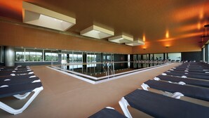 A swimming pool area with lounge chairs and a glass wall offering a view of the outdoors.