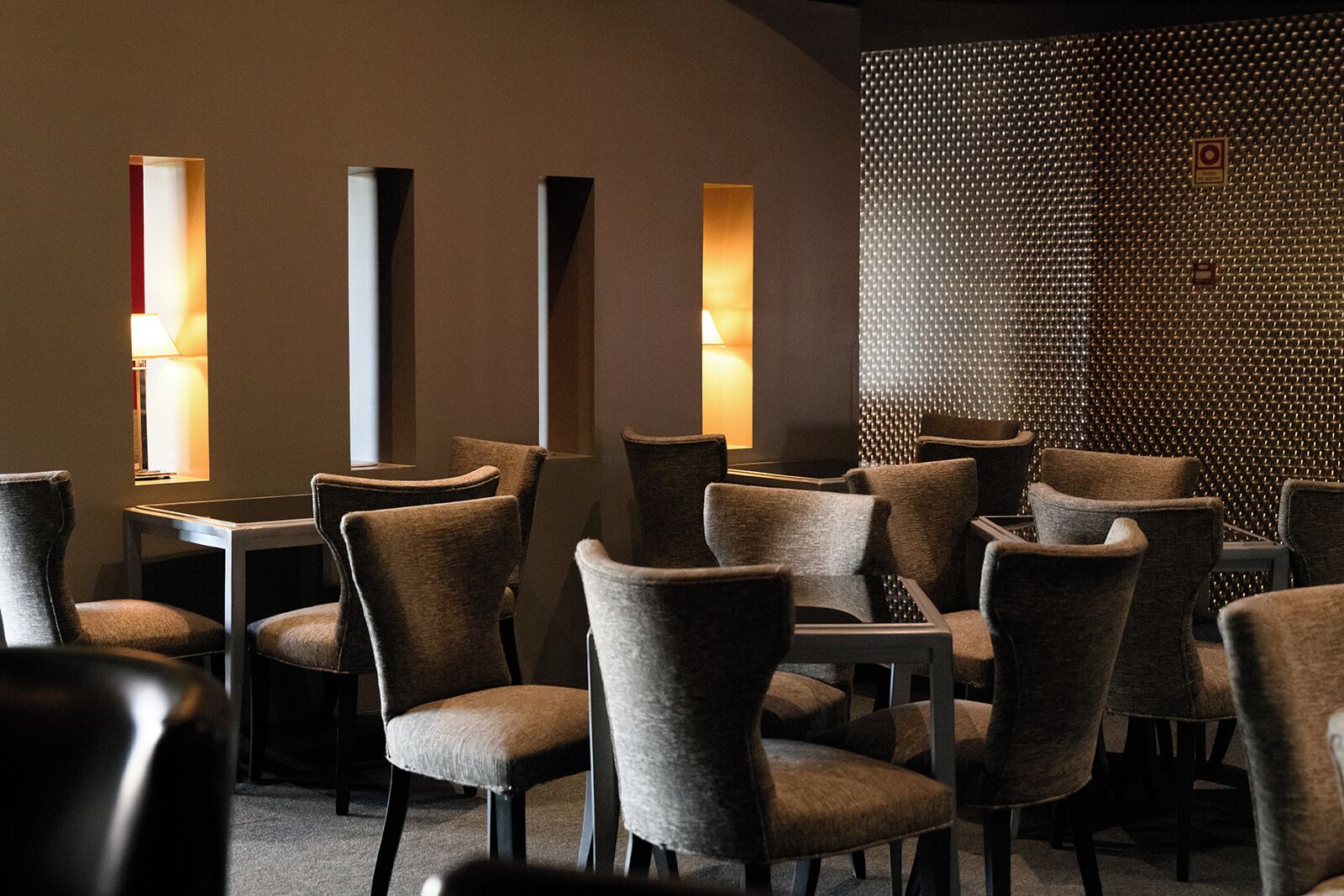 A restaurant with multiple tables and chairs, warm lighting, and a textured wall.