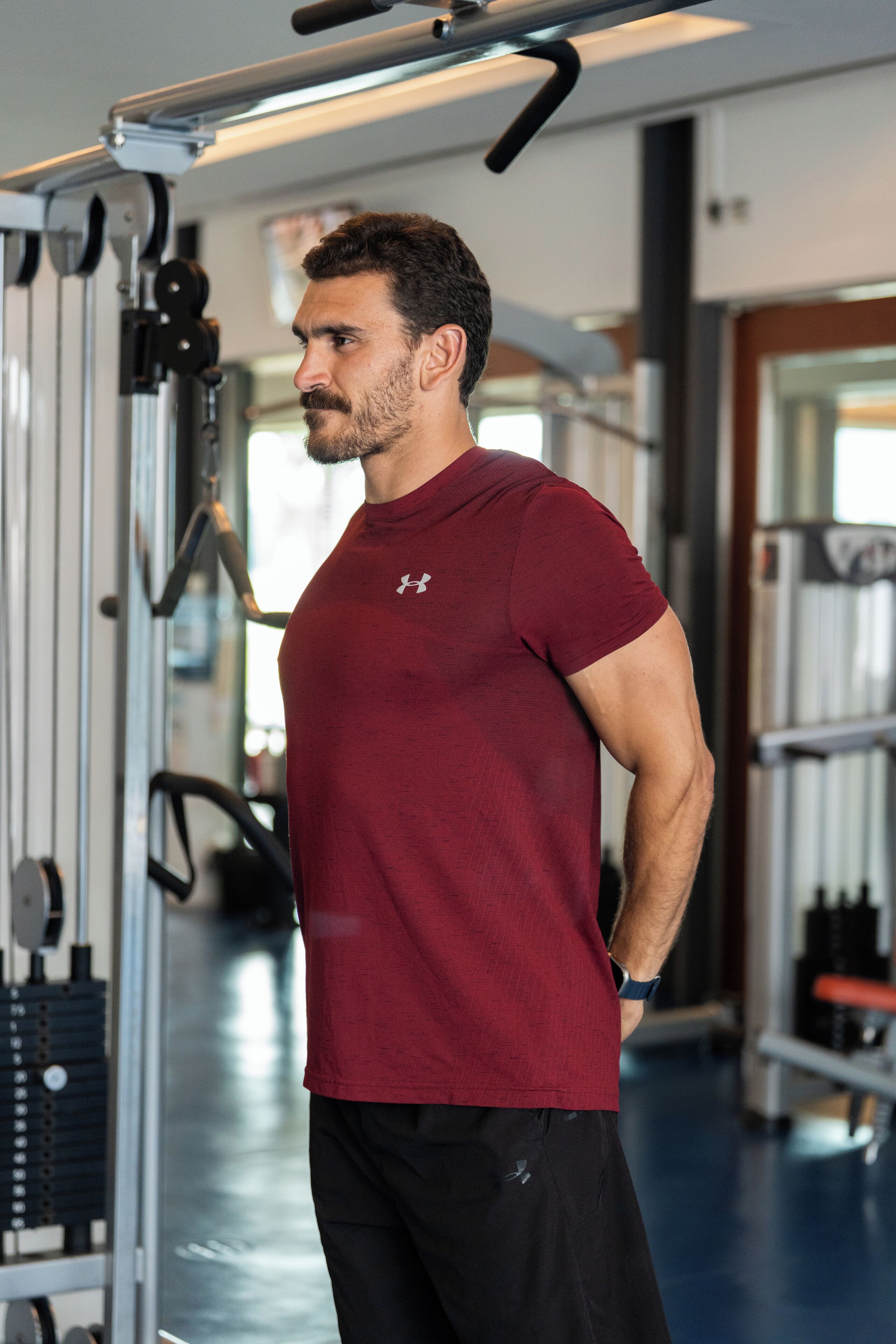 A gym with exercise equipment and a person wearing a maroon shirt and black shorts.
