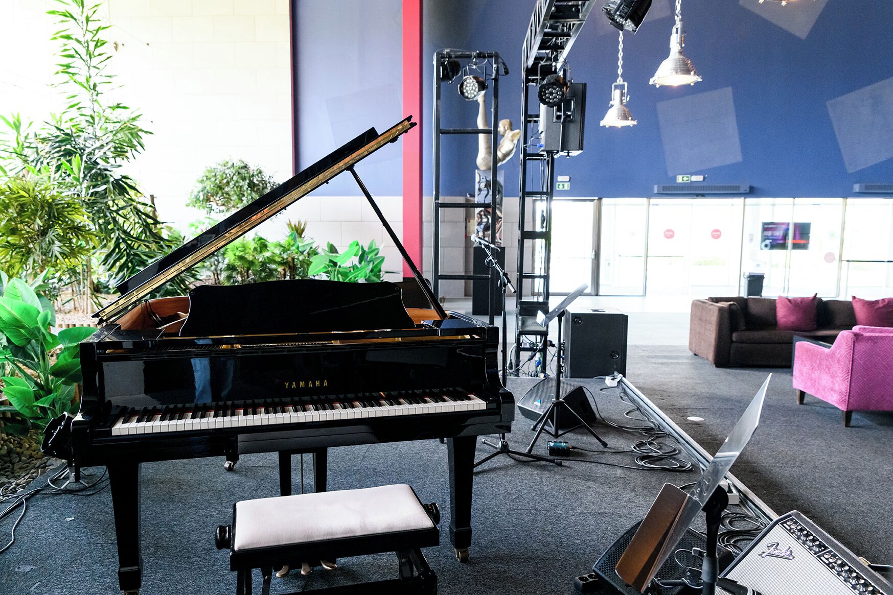 A Yamaha grand piano in an indoor setting with a stage lighting rig, a bench, and a Fender amplifier.