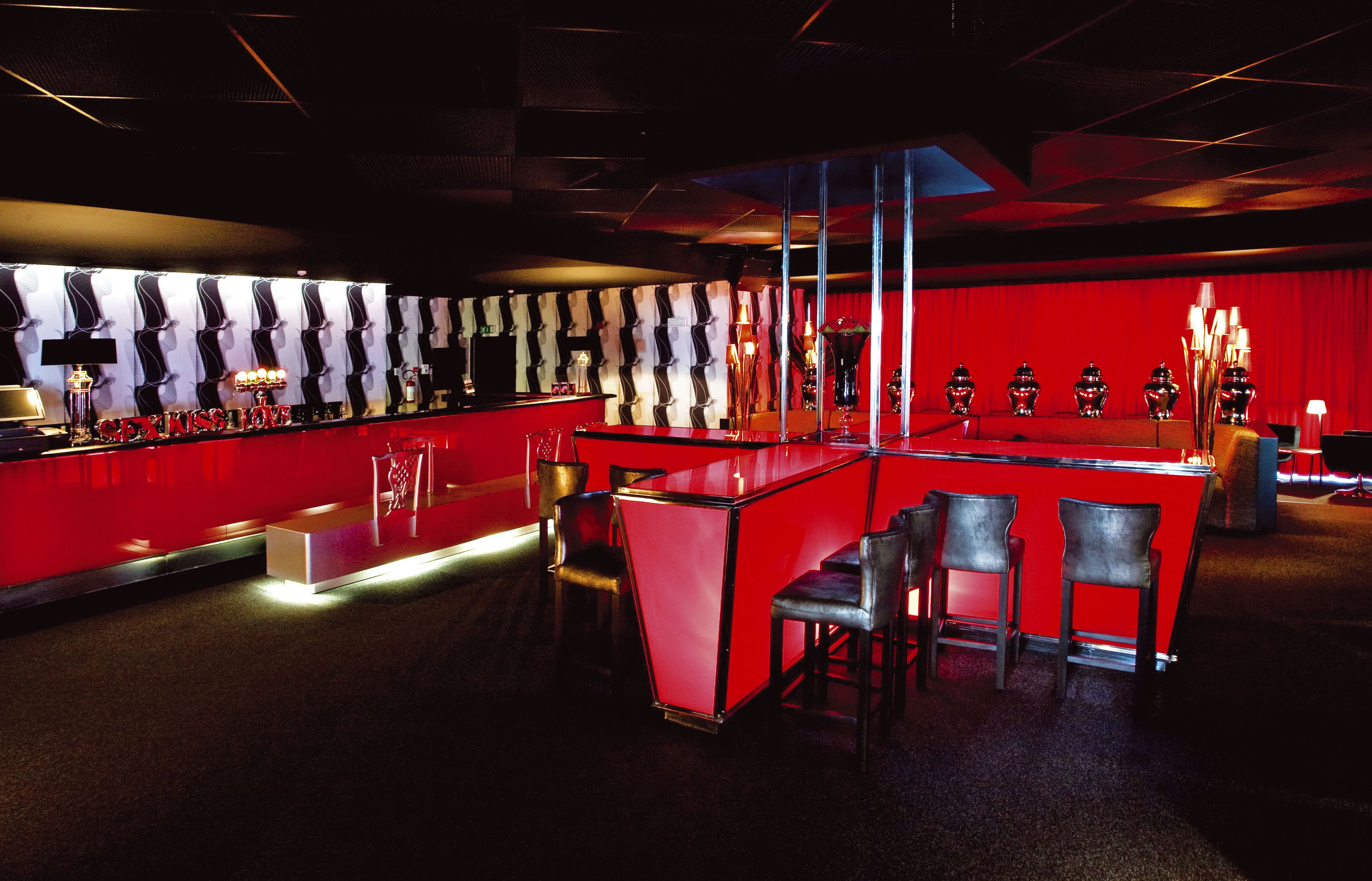 Zona de bar con mostrador rojo, sillas negras y un telón rojo de fondo.