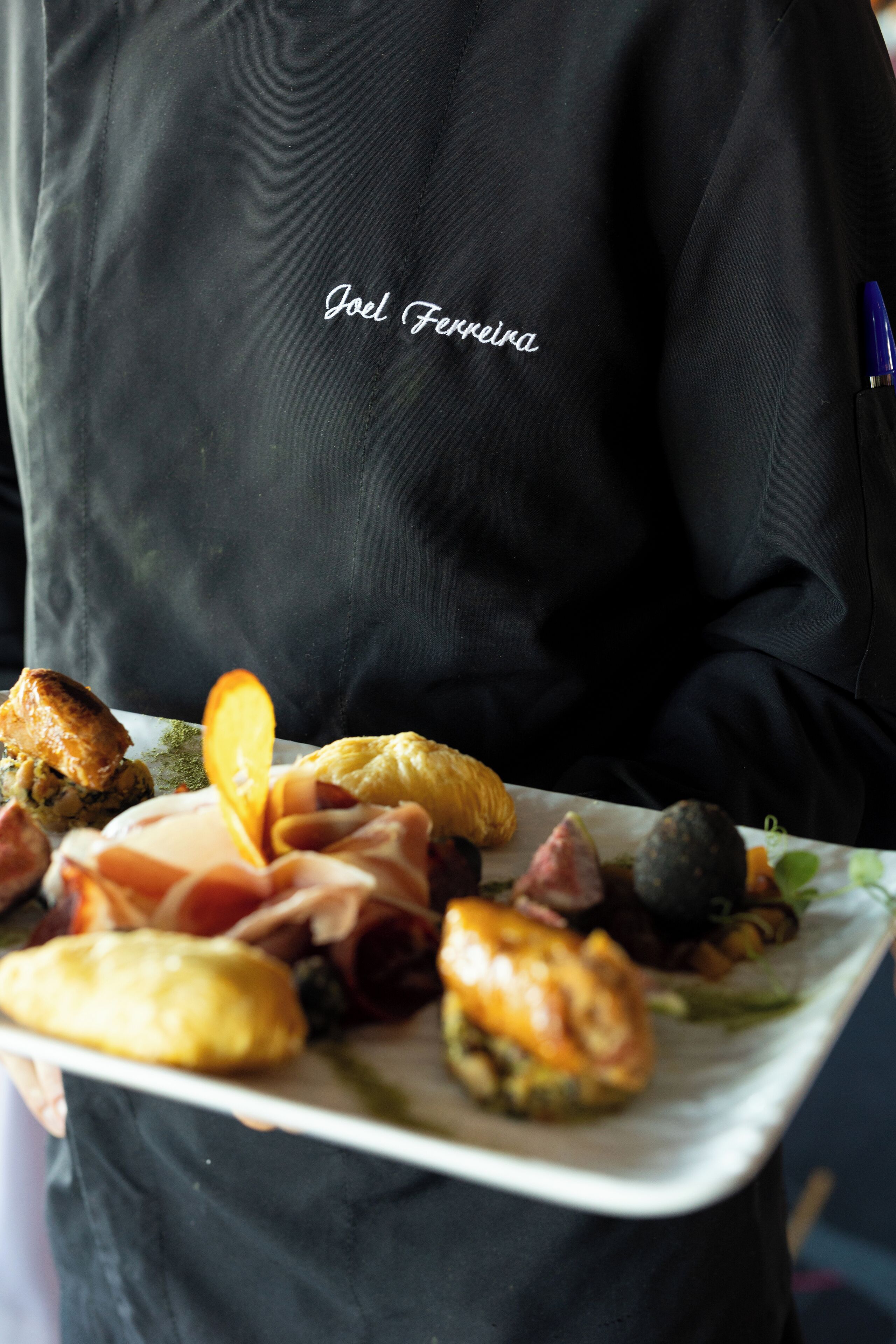 A person holding a plate with various foods, including a croissant and a piece of meat.