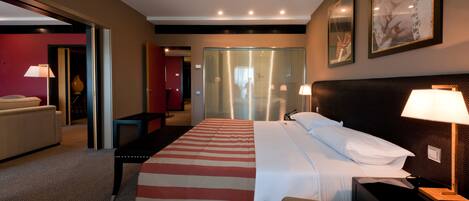 A hotel room with a bed, bedside table, lamp, and a large window with blinds.