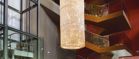 A modern interior with a large, cylindrical chandelier, glass railings, and a staircase with wooden accents.