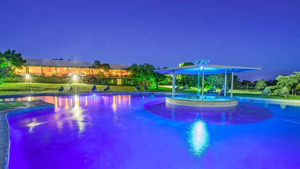 Una piscina con una fuente central, rodeada de sillas de descanso y una zona de estar techada.
