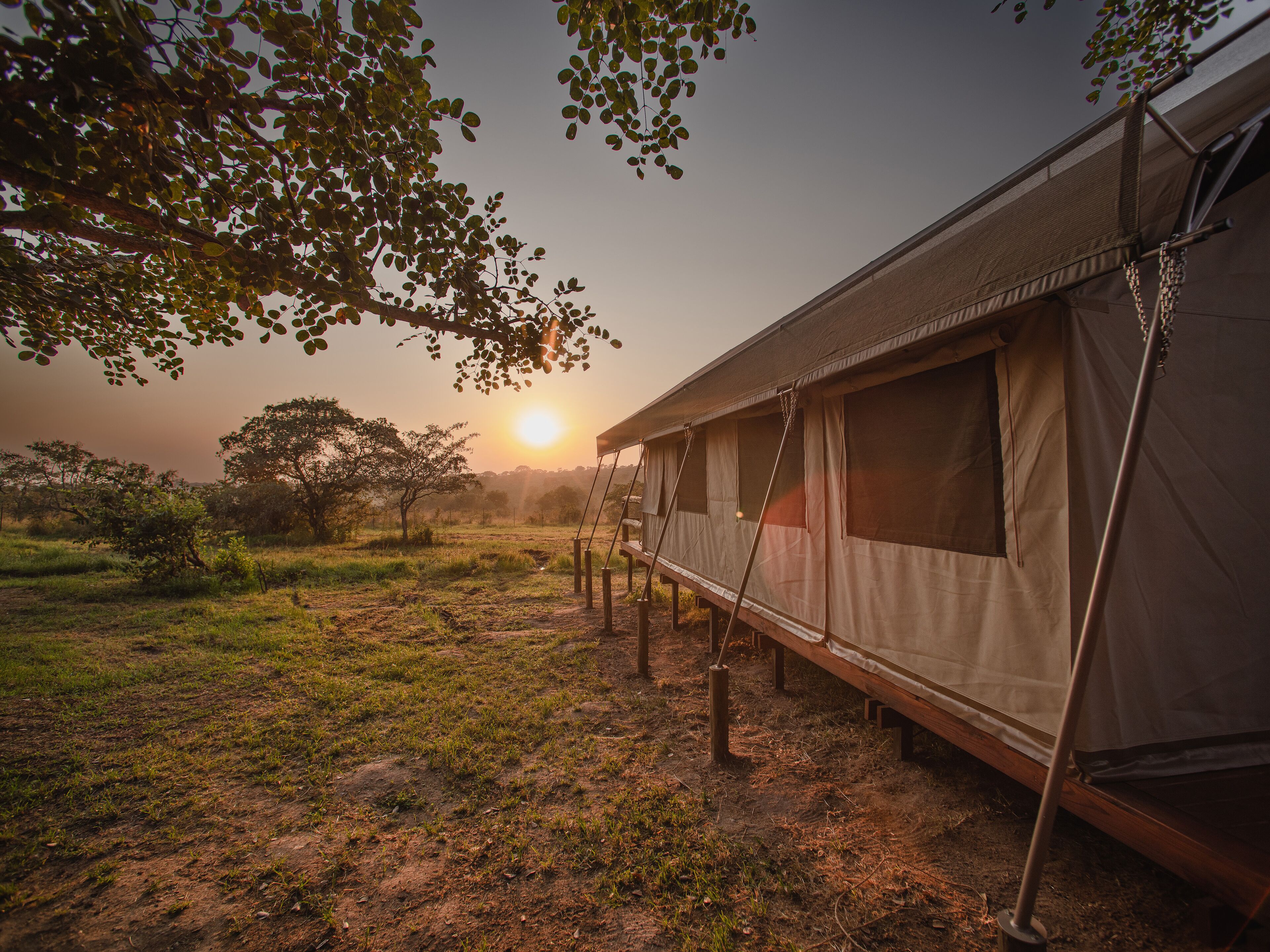 A tent with a simple, functional design, set in a natural landscape with a clear sky and sunlight.