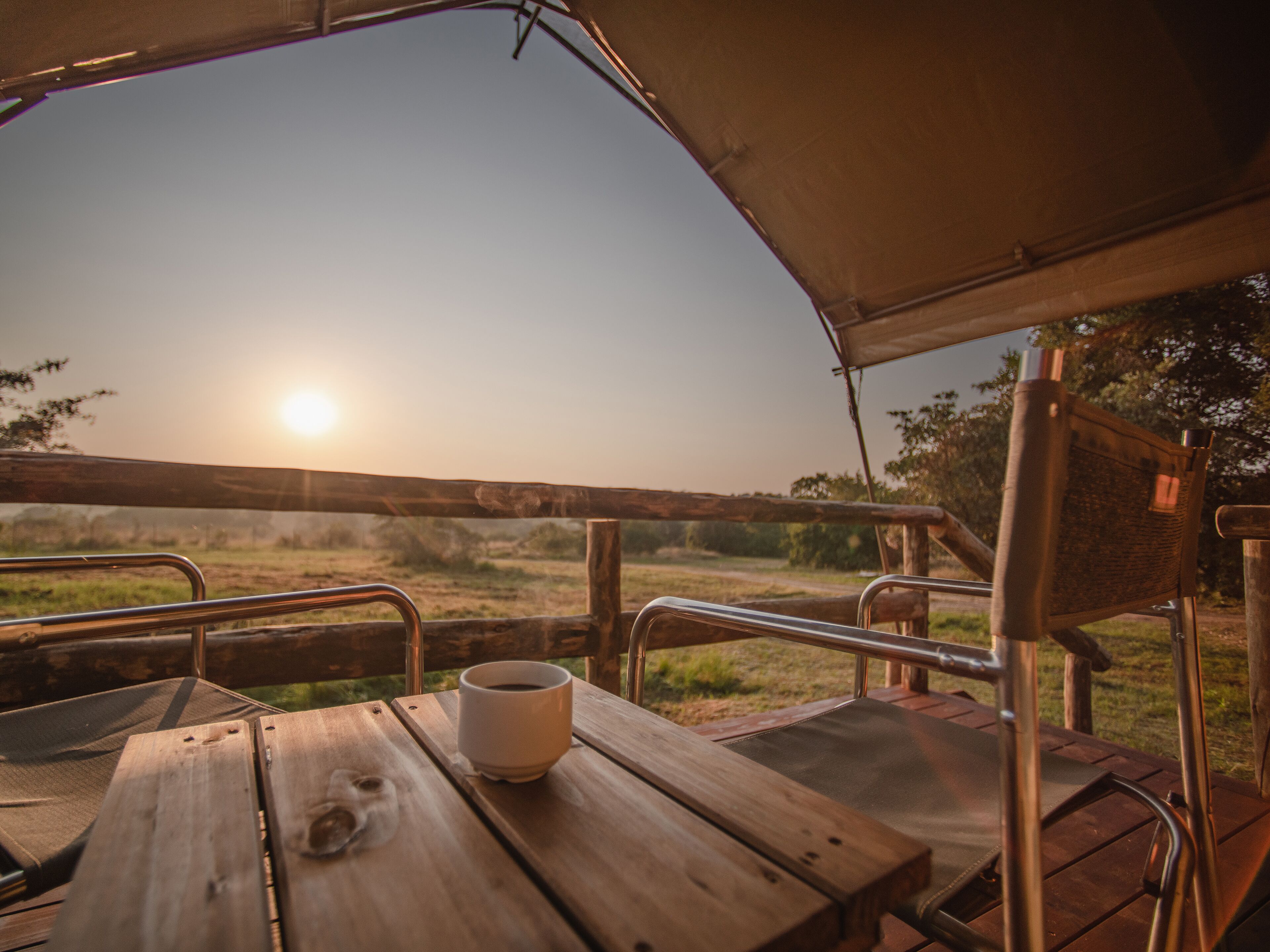 Een houten tafel met een kopje, metalen hekwerk en uitzicht op de zonsondergang.