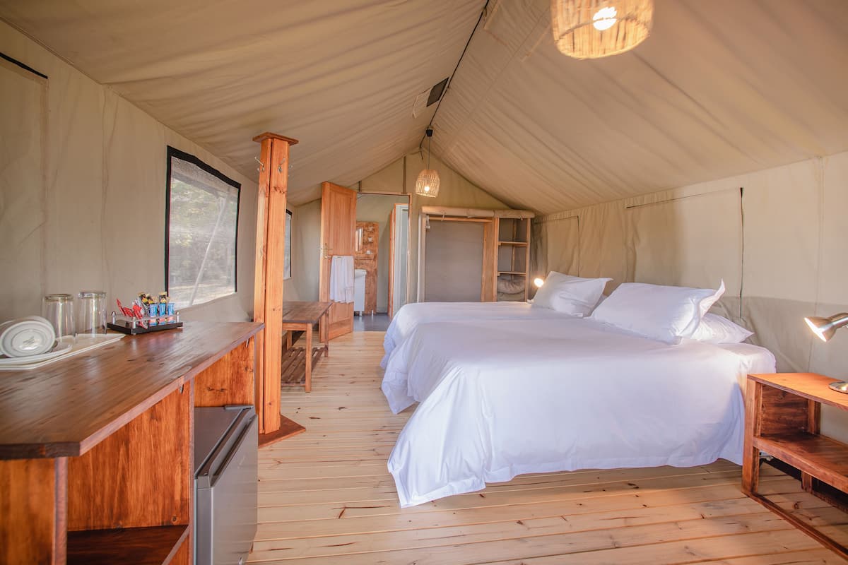 A tented accommodation with two beds, a wooden desk, and a small kitchenette.