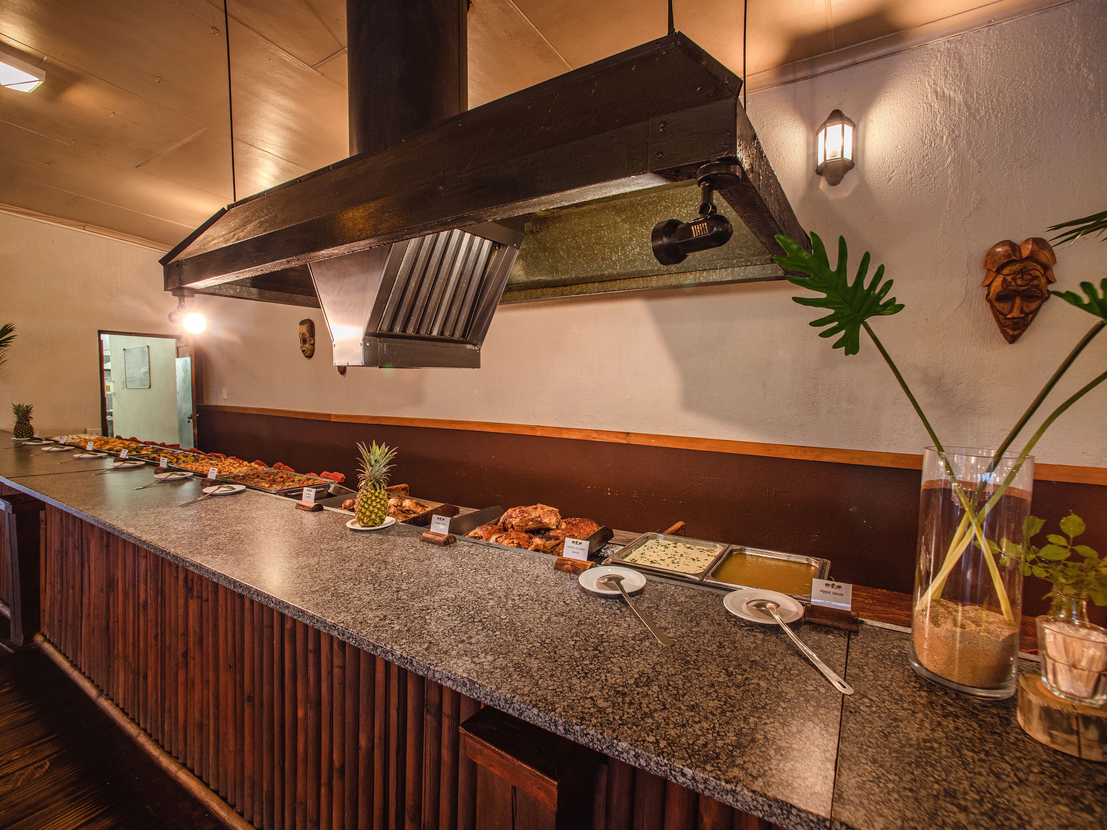 Un comptoir de buffet proposant divers plats, une grande hotte d’extraction au-dessus et un mur recouvert de panneaux en bois.