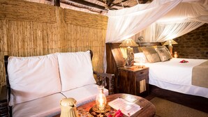 A room with a bed, a sofa, a nightstand with a lamp, and a wooden headboard. - Taita Falcon Lodge (Livingstone)