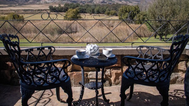 Un patio con dos sillas de metal decoradas y una pequeña mesa, con vistas a un paisaje montañoso.
