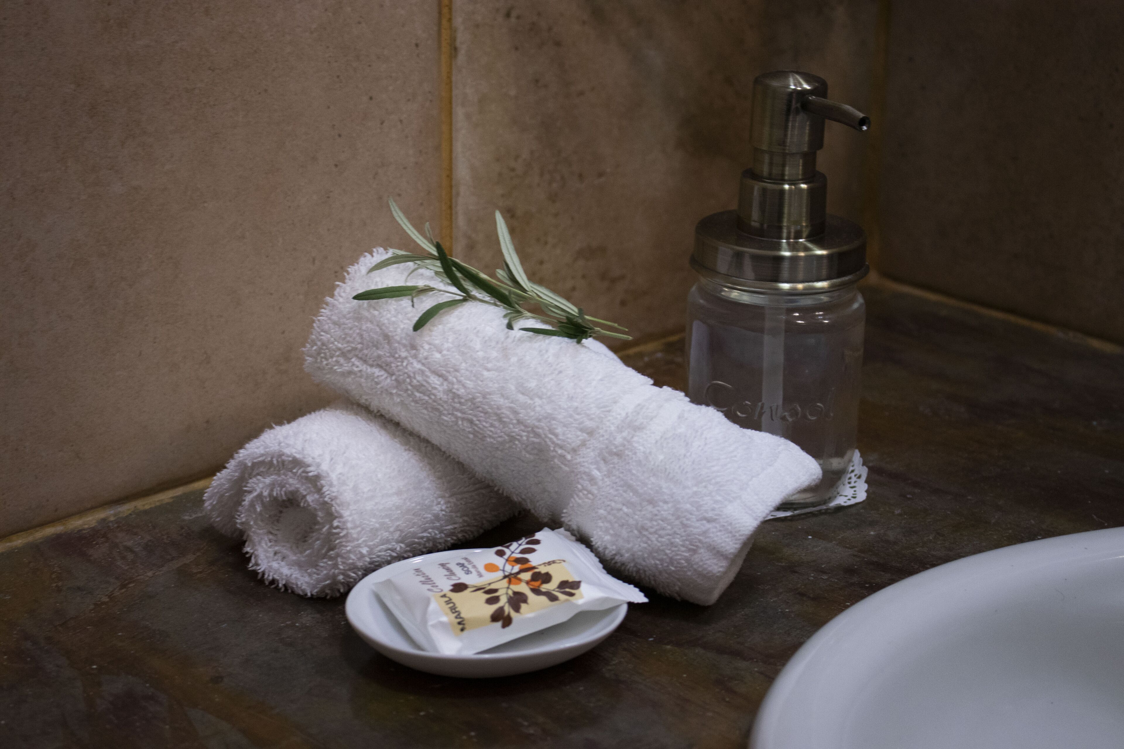 A bathroom with a towel, a bottle of liquid soap, and a small dish with a sachet.